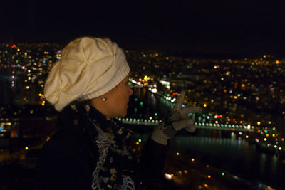 Woman gesturing by illuminated city against sky at night