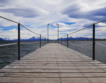 Wood pier with a cloudy sky and snow capped mountains in the background