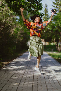 Happy asian woman in energetic jumping in summer green park.