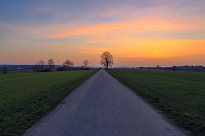 Road amidst field against sky during sunset