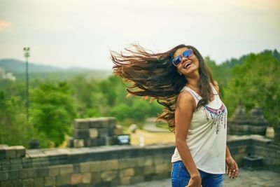 Smiling woman with tousled hair standing against sky