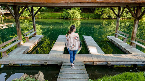 Rear view of woman standing on deck of boathouse on river.