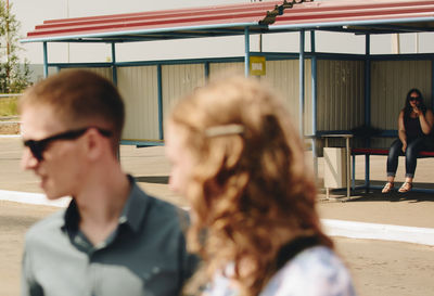 Close-up of friends with woman sitting on bench at bus stop