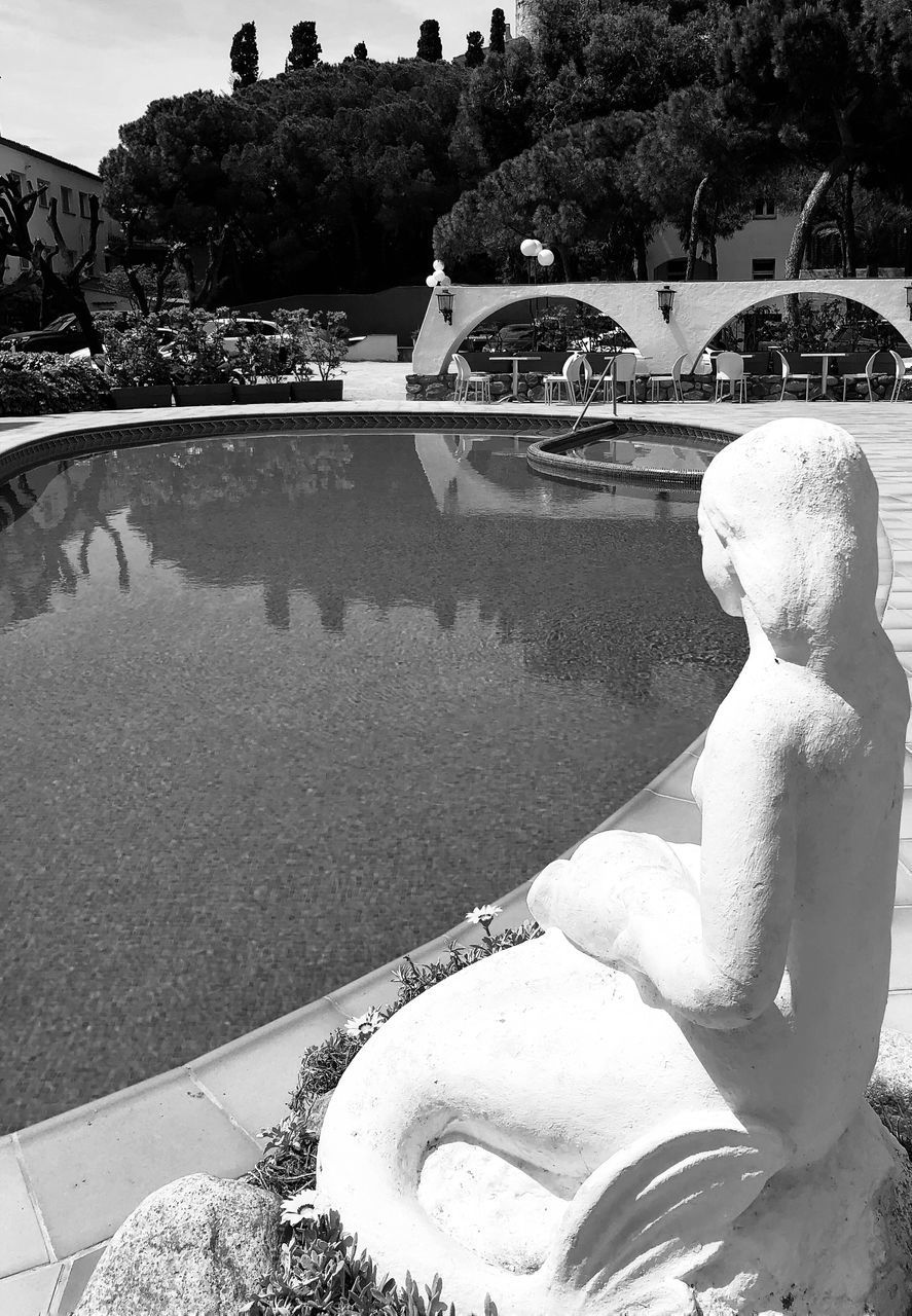 STATUE BY SWIMMING POOL AGAINST TREES