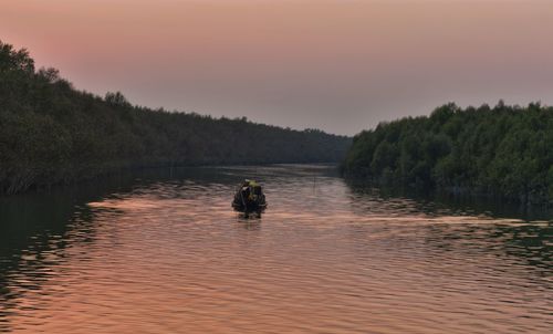 Man on boat in lake against sky during sunset