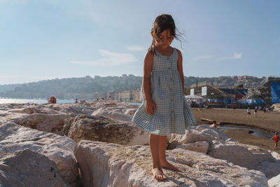 Side view of girl standing on rock by sea against sky