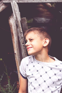 A boy stands near an old wooden booth and looks up squinting