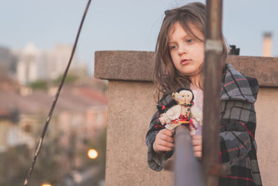 Thoughtful girl holding toy on railing in balcony