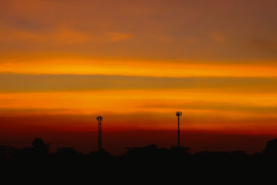 Silhouette of factory against orange sky