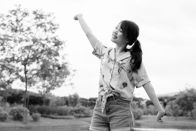 Woman with arms raised standing against sky