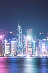 Illuminated buildings by sea against sky at night