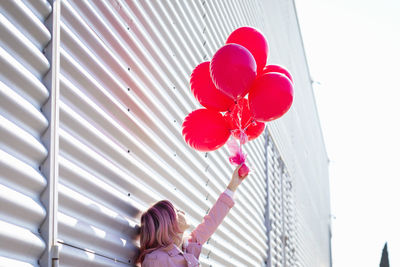 Rear view of woman with red balloons against wall