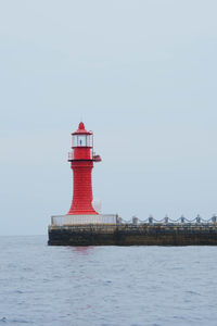 Lighthouse by sea against clear sky