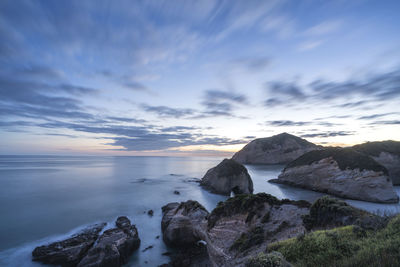 Rocks by sea against sky during sunset