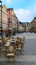 Empty chairs and tables at sidewalk cafe against buildings in city