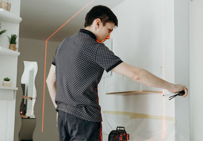 A young man checks the levelness of a shelf with a laser level.