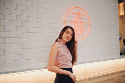 Portrait of smiling young woman standing against wall