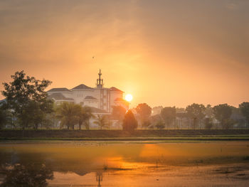 Scenic view of lake by buildings against sky during sunset