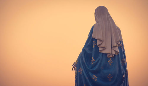 Rear view of women standing on cross against sky during sunset