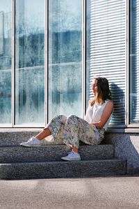 Side view of woman sitting on window