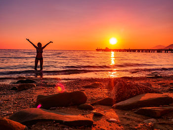 Silhouette woman standing on beach against sky during sunset