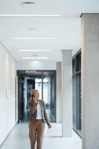 Businesswoman talking on mobile phone at office corridor