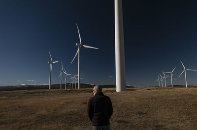Adult man in winter cloth with modern windmills against blue sky. shot in castilla la mancha, spain