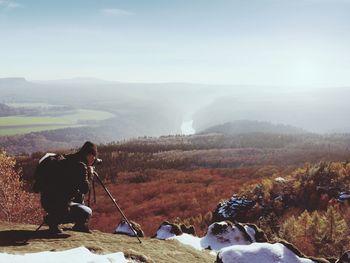 Professional photographer takes photos with camera and tripod on snowy peak. beautiful valley below