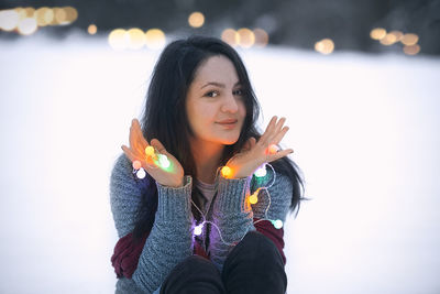 Portrait of young woman holding illuminated christmas lights during sunset