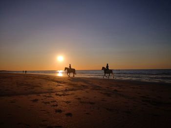 Silhouette people on beach against sky during sunset