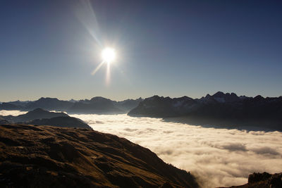 Sun shining over clouds covering mountains