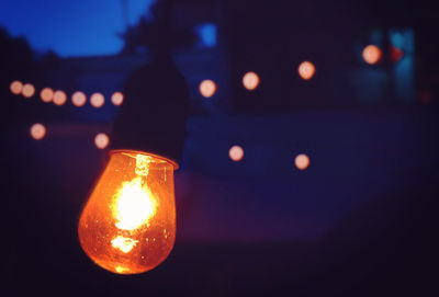 Close-up of illuminated light bulb against sky at night