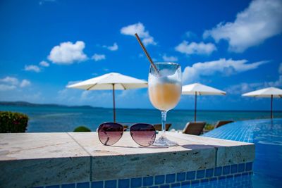 Wine glass on table by swimming pool against sea