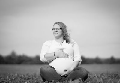 Portrait of woman sitting on field against sky