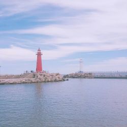 Lighthouse by sea and buildings against sky