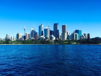 Sea by cityscape against clear blue sky