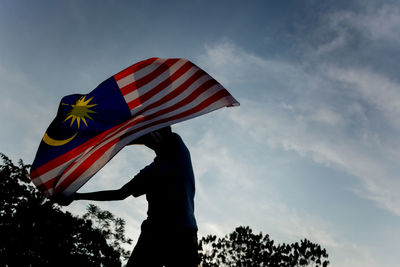 Low angle view of man waving malaysian flag against sky