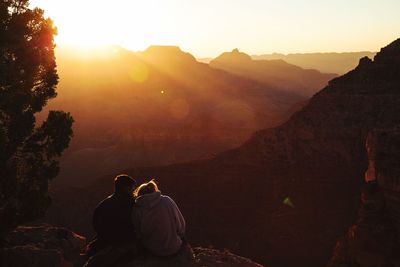 Rear view of people sitting on mountain during sunset