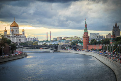 Buildings by river against cloudy sky