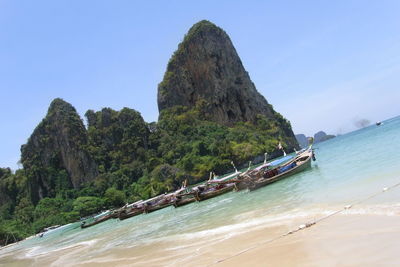 Tilt shot of longtail boats moored on shore at beach against sky