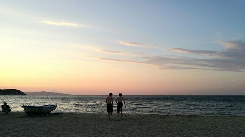 Rear view of shirtless boys against sky during sunset