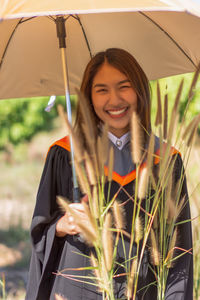 Portrait of happy young woman with umbrella standing on field 
