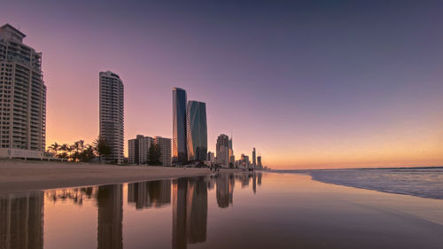 Reflection of buildings in swimming pool against sky during sunset