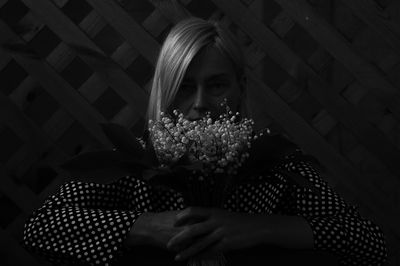 Close-up of woman holding flowers against black background