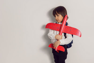 Boy child in a white shirt and jeans flies on a red airplane toy at the white wall of the house