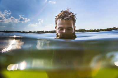 Man swimming in lake against sky during sunny day