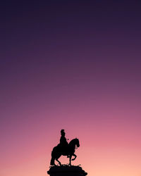 Silhouette man riding statue against sky during sunset