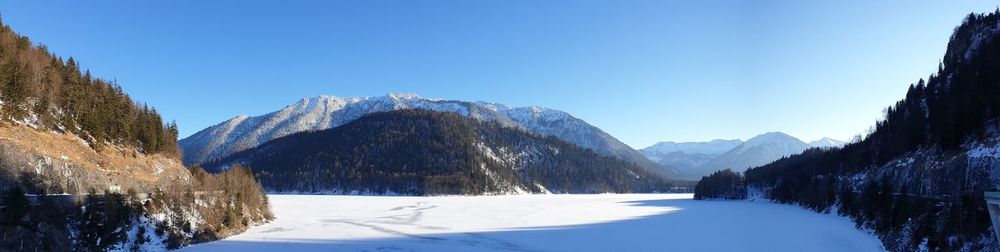Panoramic view of snowcapped mountains against clear blue sky with frozen lake