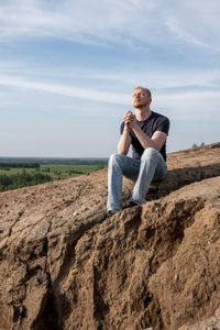 Young woman sitting on rock against sky