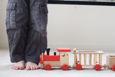 Low section of child standing by toy train on floor